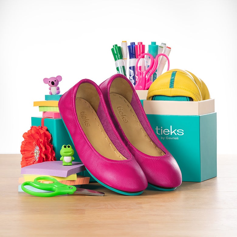 fuchsia pink tieks flats on a table with school supplies
