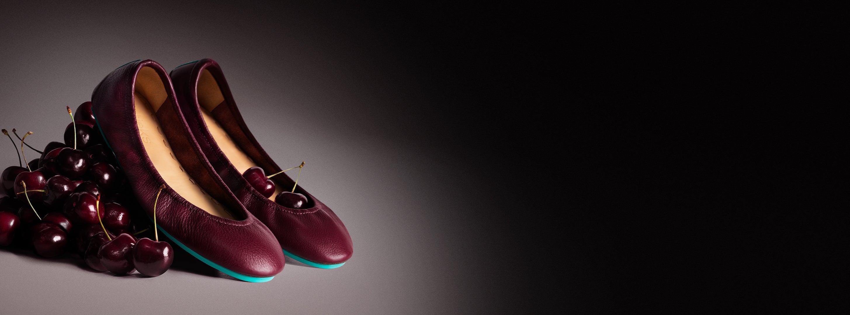 burgundy ballet flats sitting on a pile of cherries. 