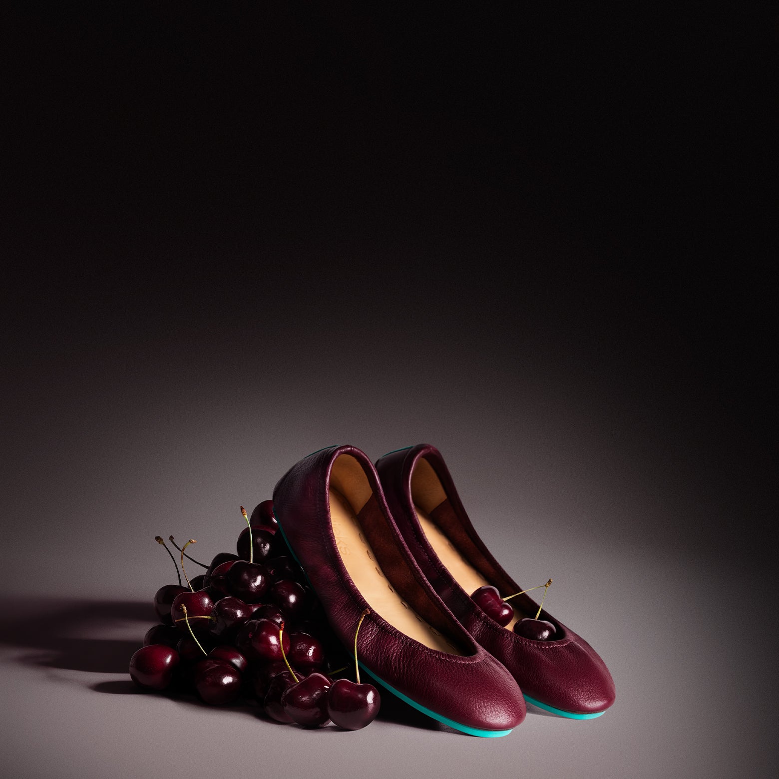 burgundy ballet flats sitting on a pile of cherries. 
