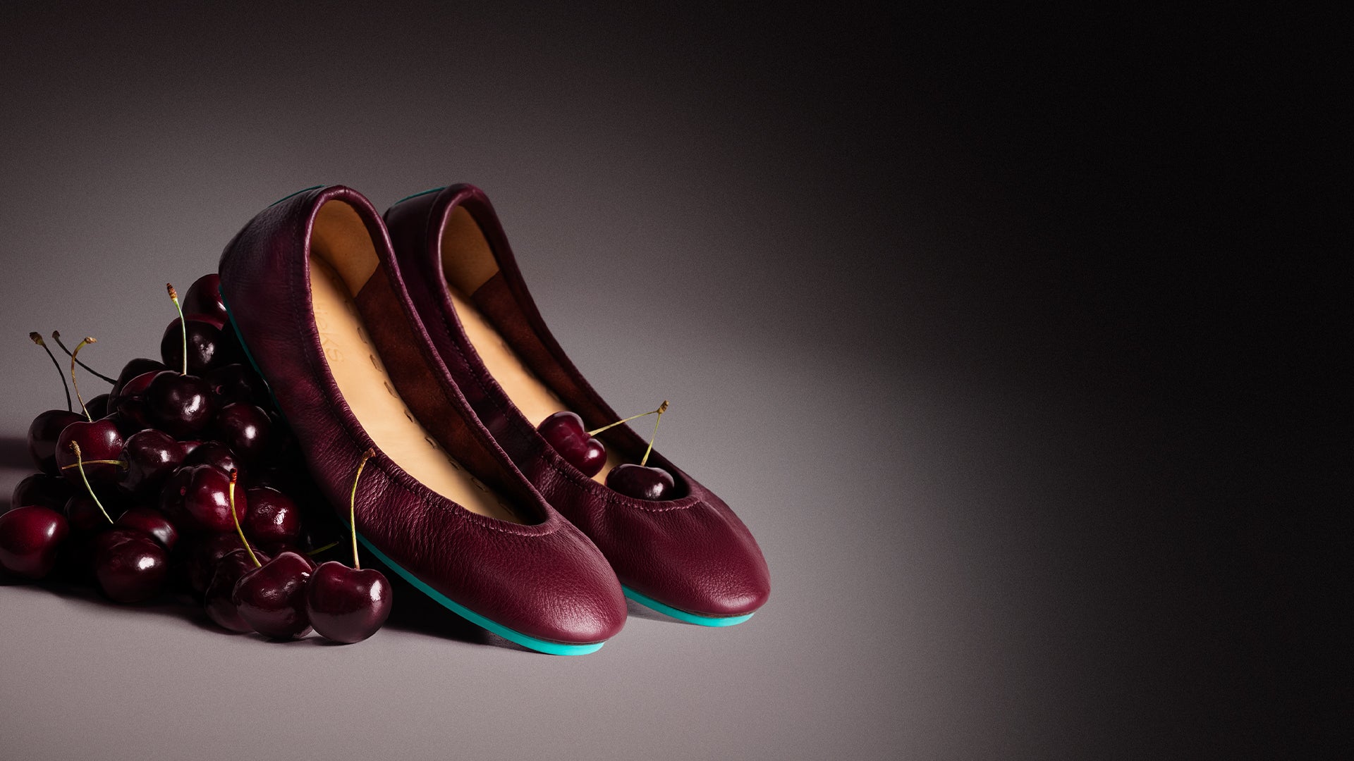 burgundy ballet flats sitting on a pile of cherries. 