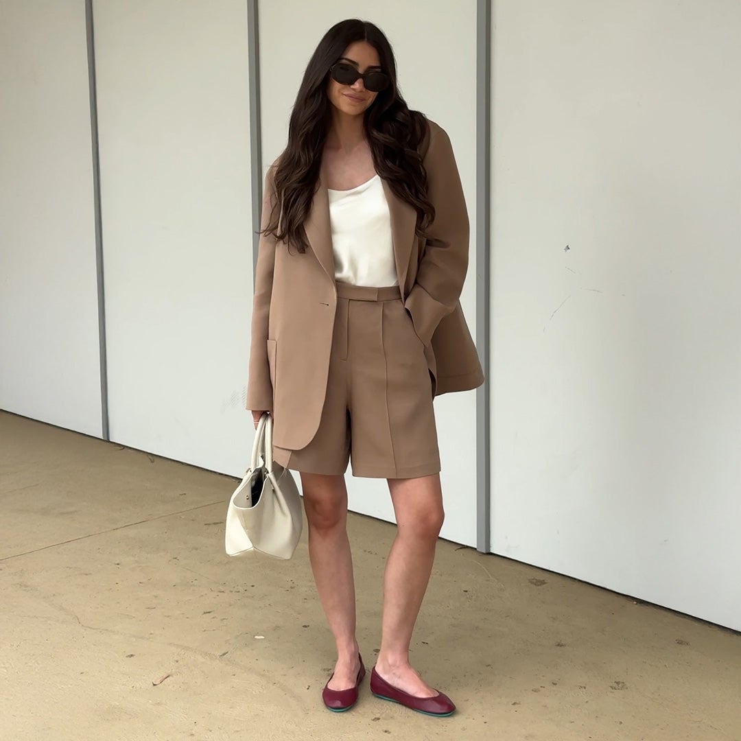 woman wearing burgundy tieks flats with taupe colored blazer and shorts