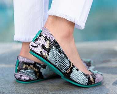 model wearing white pants and lavender snake tieks flats