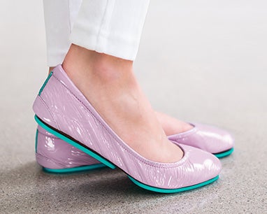 woman wearing white pants and lavender patent tieks flats