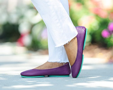 model wearing white pants and lilac tieks flats in a garden