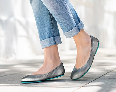 model wearing jeans and metallic pewter tieks flats in a city background