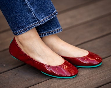 ruby red tieks flats paired with jeans on a wooden deck