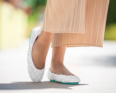 model wearing tan pants and white rose tieks flats