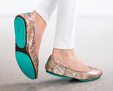 model wearing white pants and wild copper tieks flats